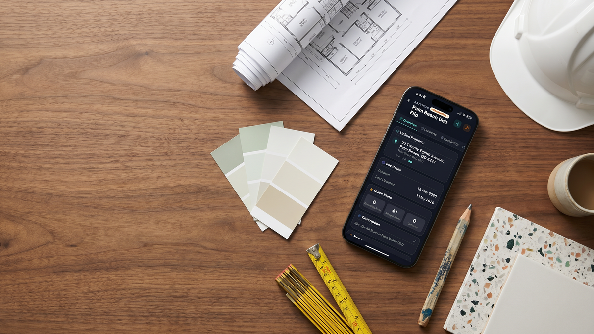 iPhone showing the FlipPro AI Palm Beach Unit Flip project overview, surrounded by floorplans, paint swatches, tile samples and a builder's pencil on a walnut workbench